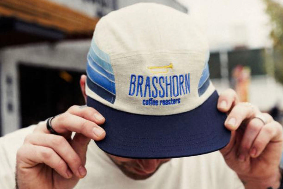 Person holding a cap with 'BRASSHORN coffee roasters' branding.