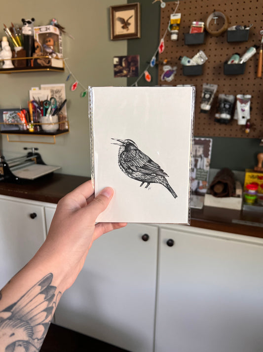 Matted illustration of a bird held by a person in a workshop setting