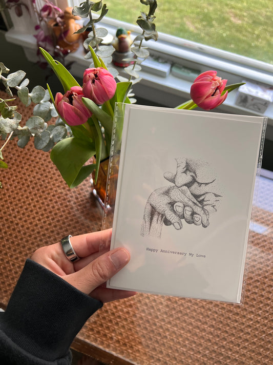 Hand holding a card with a drawing of two people holding hands and the man is kissing the women's hand.