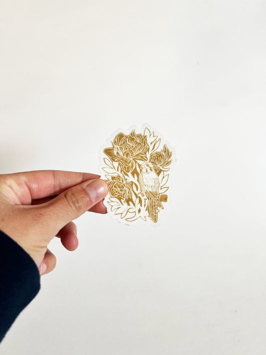 Hand holding a gold floral and bird design against a white background