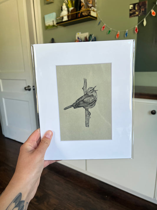 A hand holding a framed bird drawing.