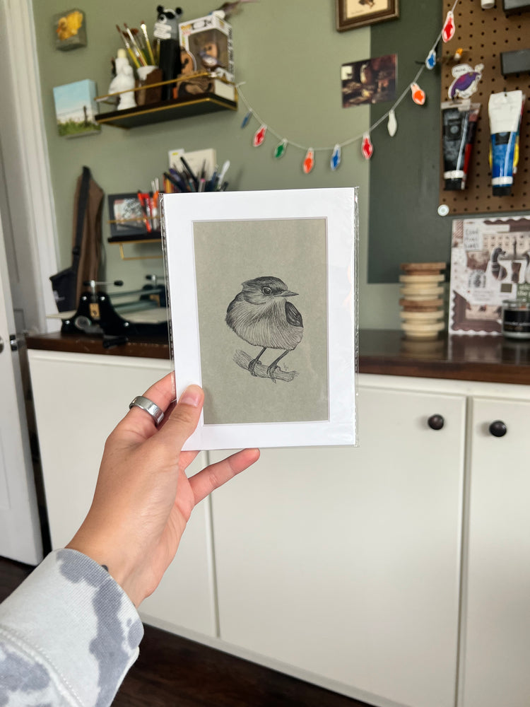 A hand holding a matted bird drawing.