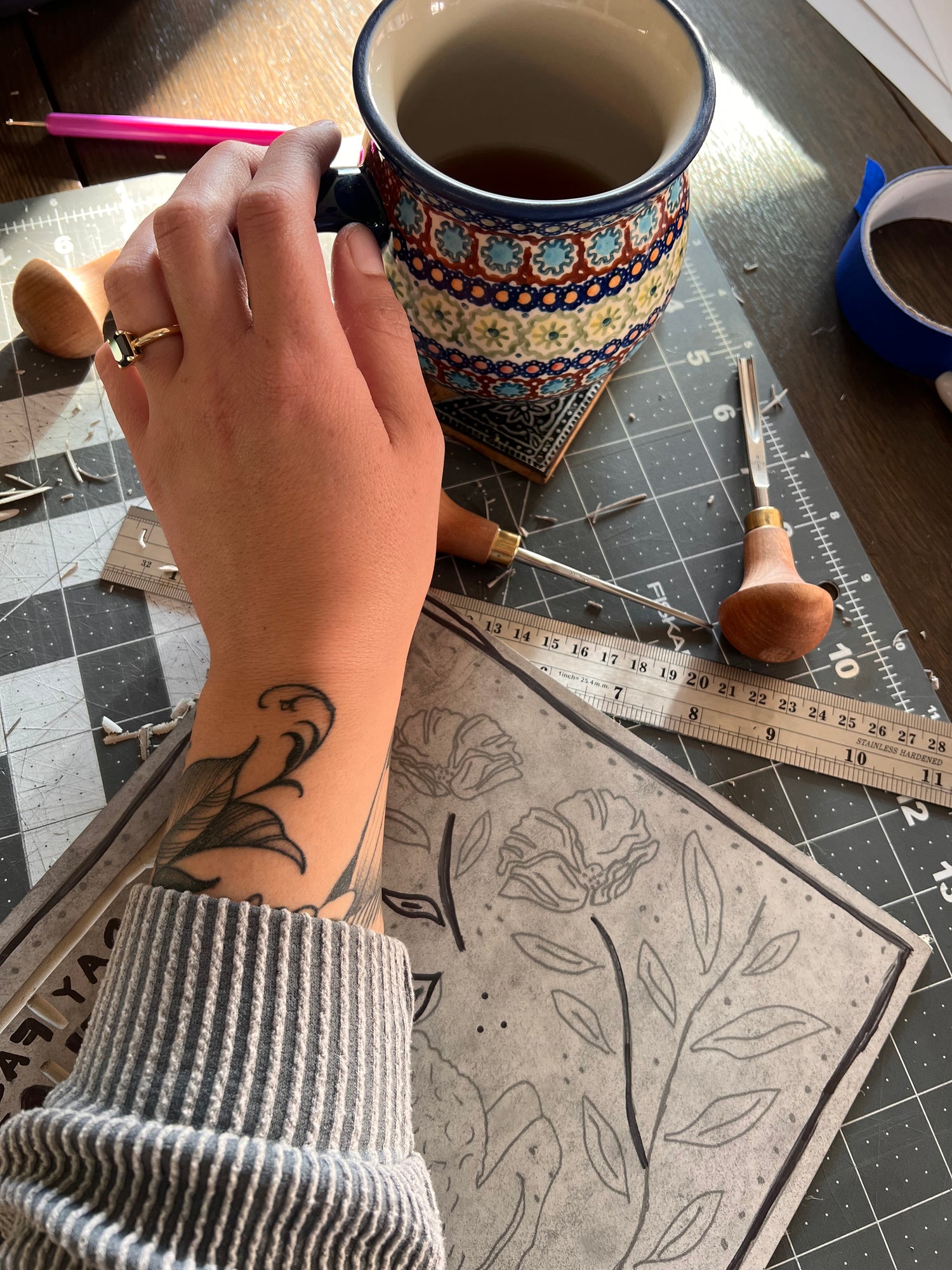 Photo of Emily Ciecka reaching for her coffee over her work in progress linocut