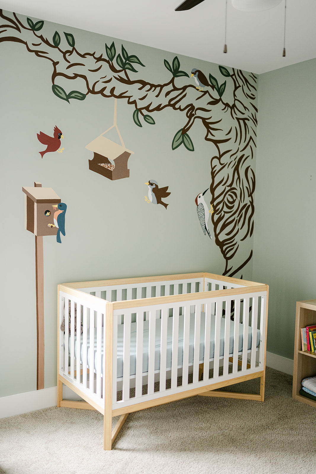 Nursery room with a crib, wall decals of birds and trees, and a small mailbox.