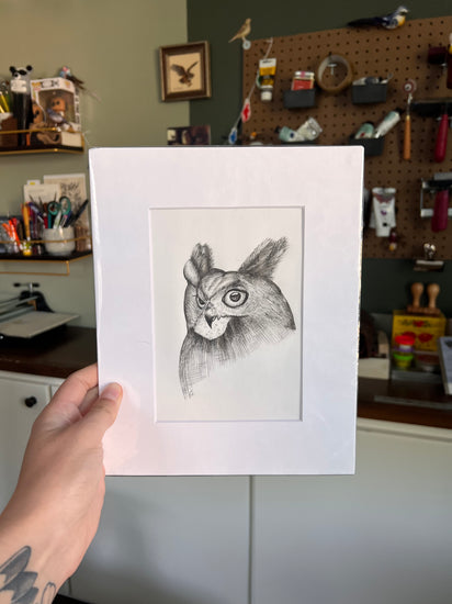 Matted illustration of a bird held by a person in a workshop setting