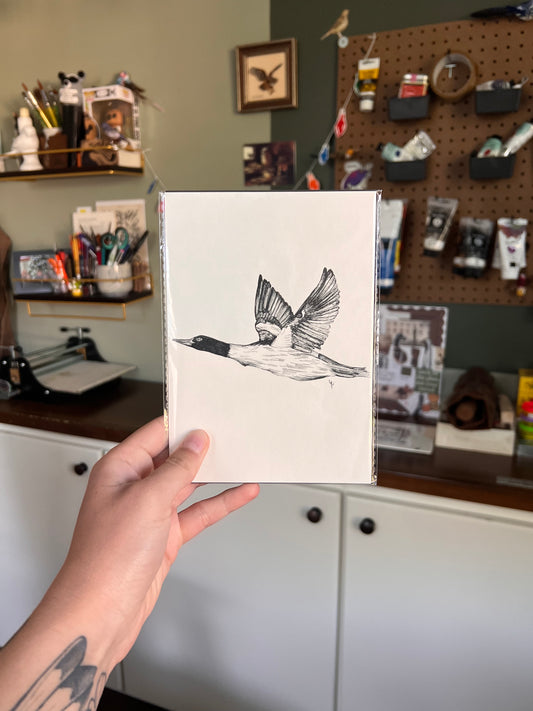 Matted illustration of a bird held by a person in a workshop setting