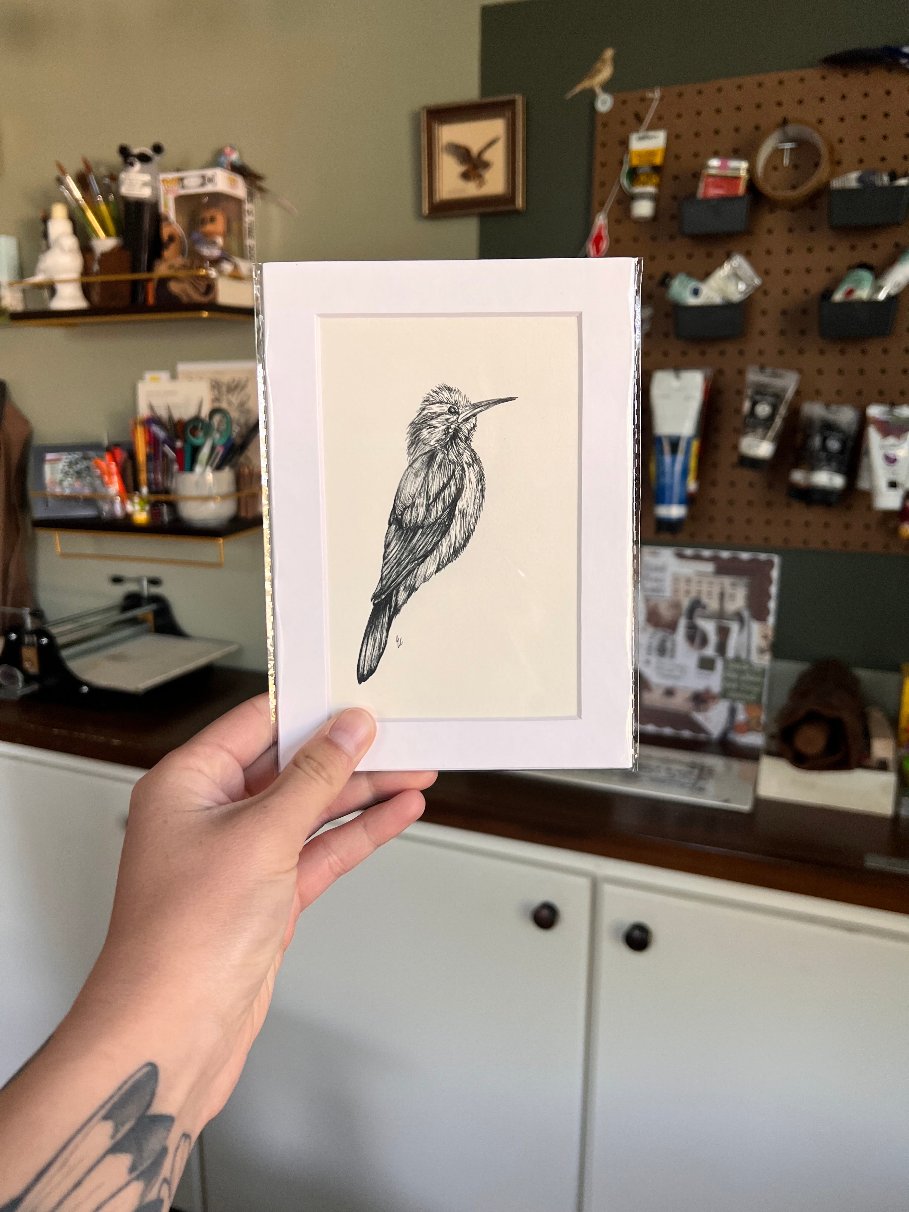 Matted illustration of a bird held by a person in a workshop setting