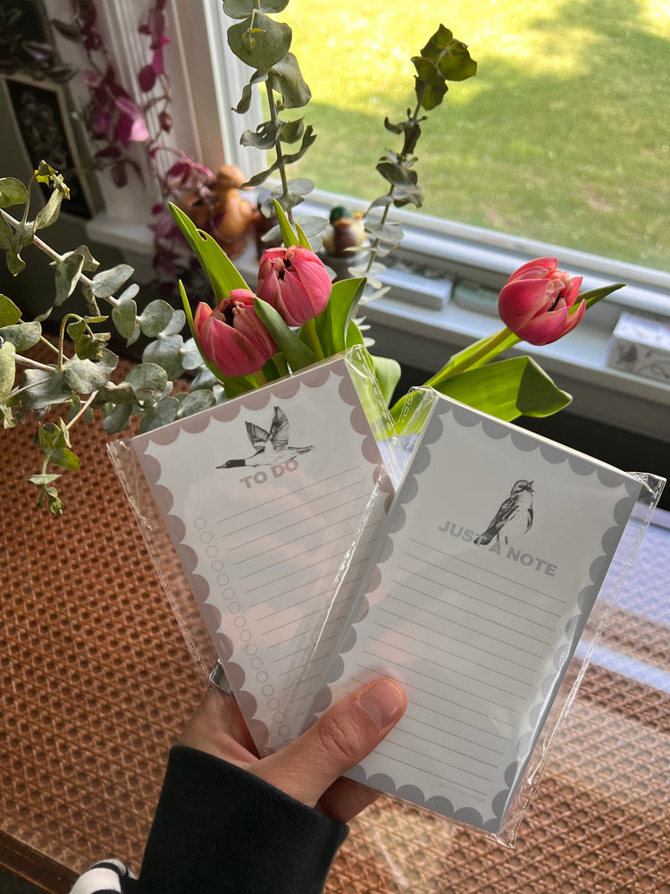 Hand holding a set of stationery with flowers and a window in the background