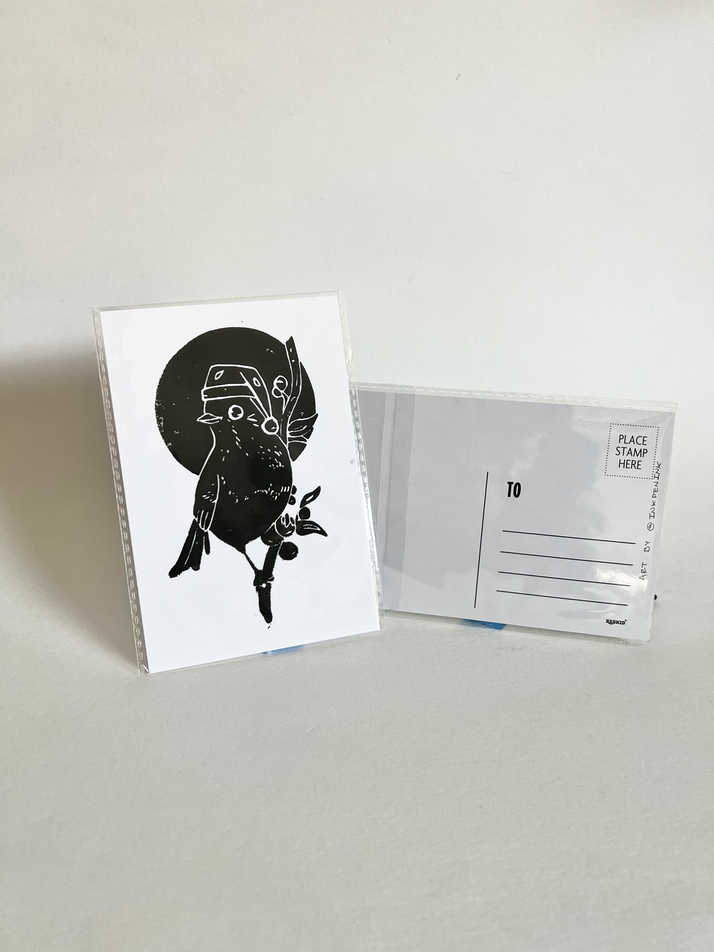 Greeting card with black and white illustration of a bird wearing a hat, next to an envelope on a light gray background.