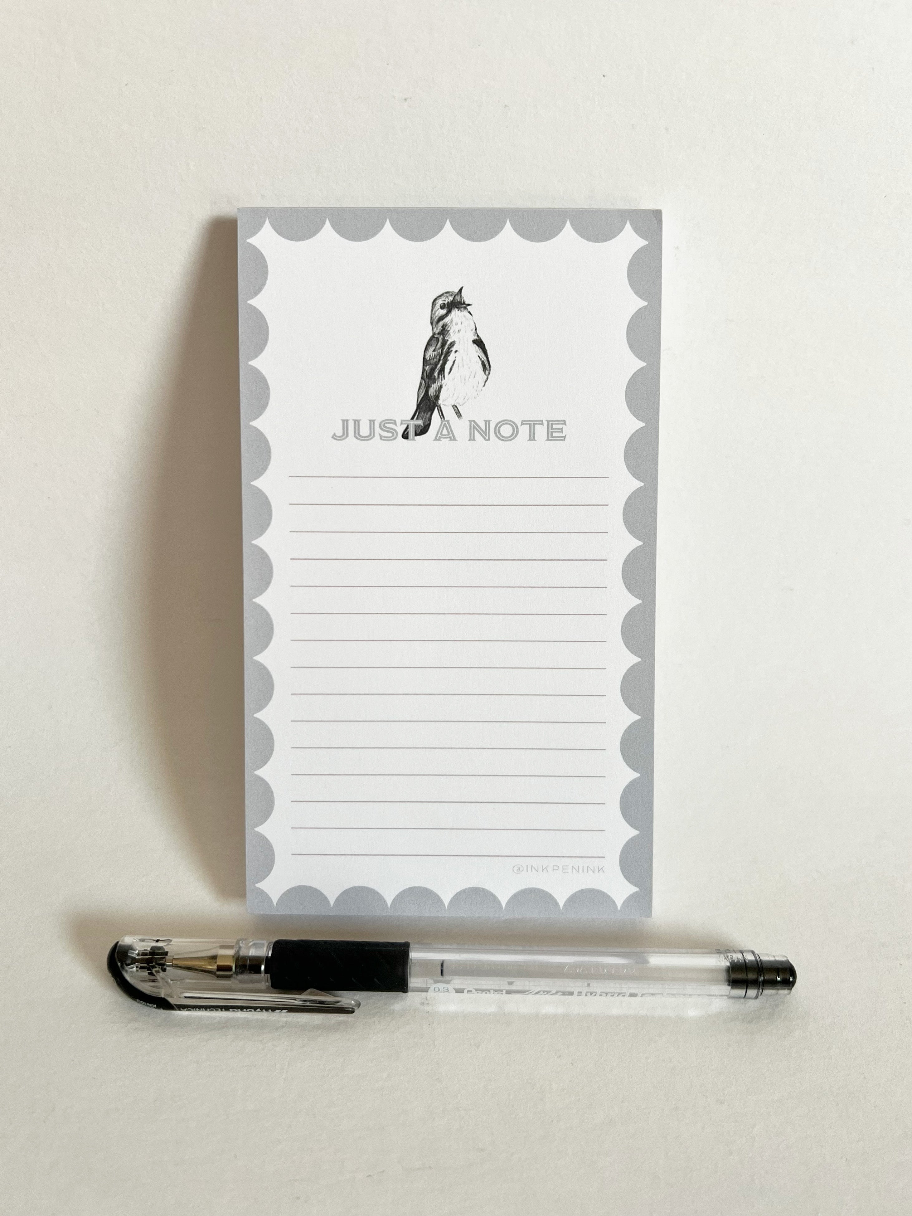Notepad with 'Just a Note' text and penguin illustration, accompanied by a pen on a light background