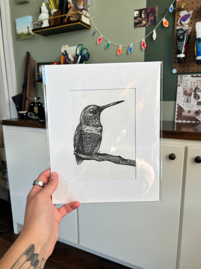 A hand holding a framed bird drawing.