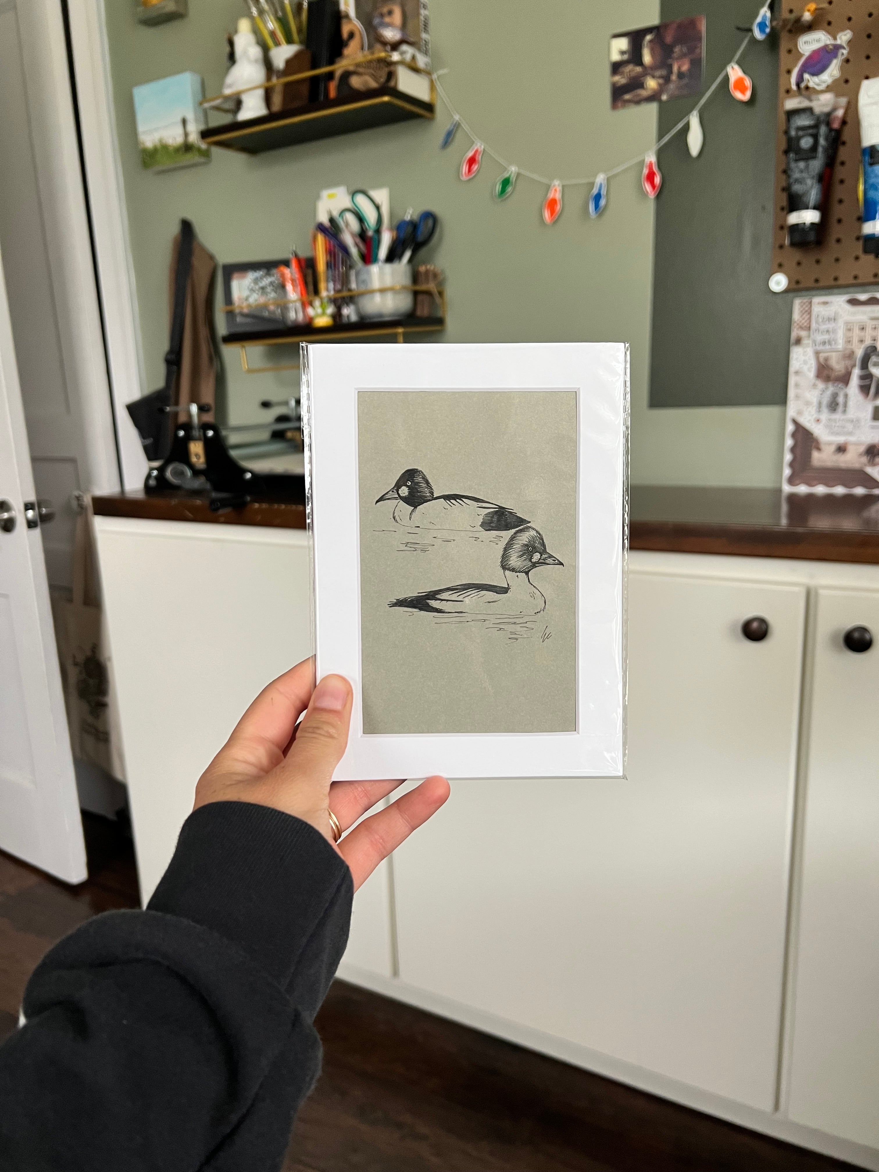 A hand holding a matted bird drawing.