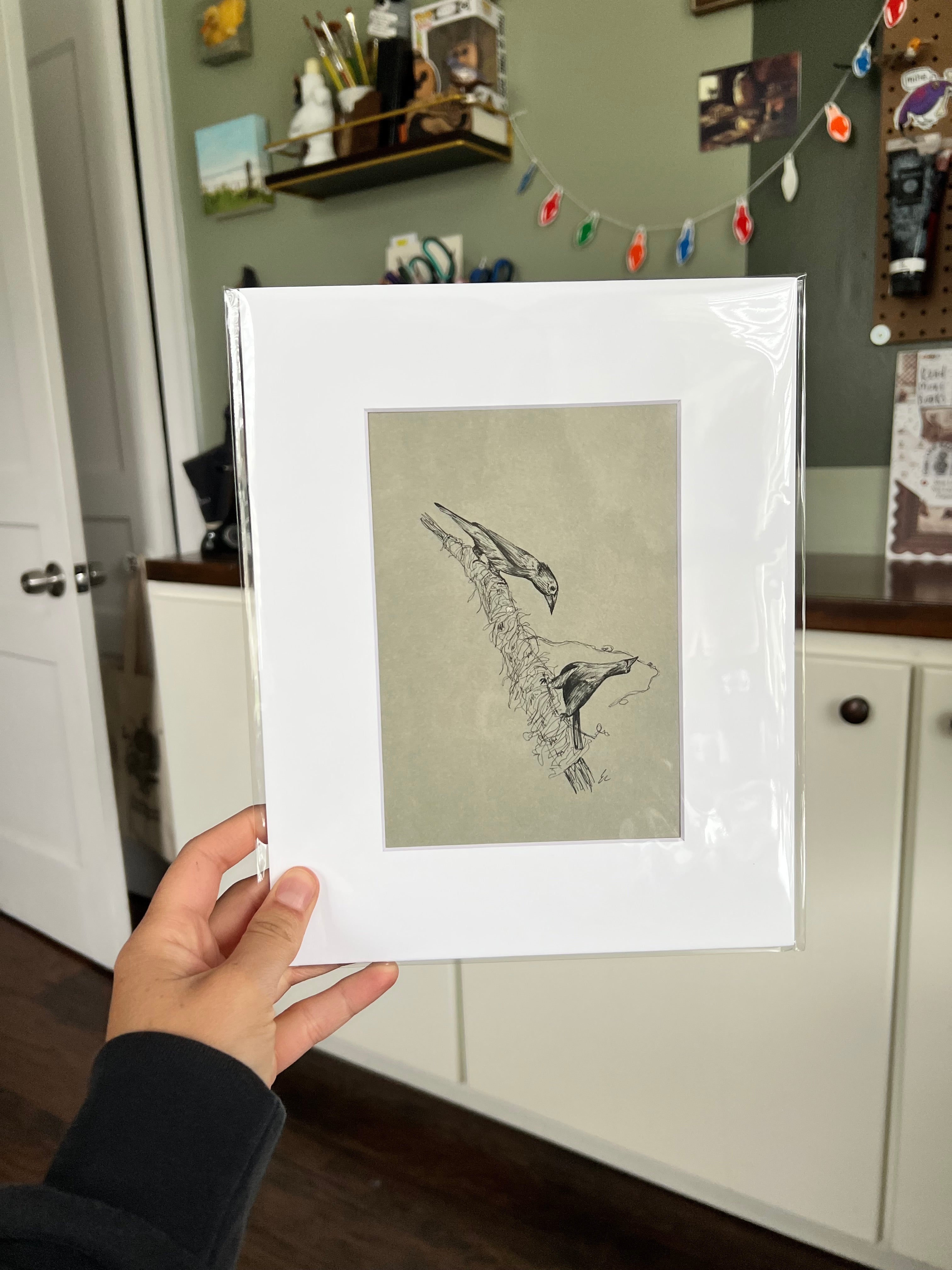 A hand holding a matted bird drawing.