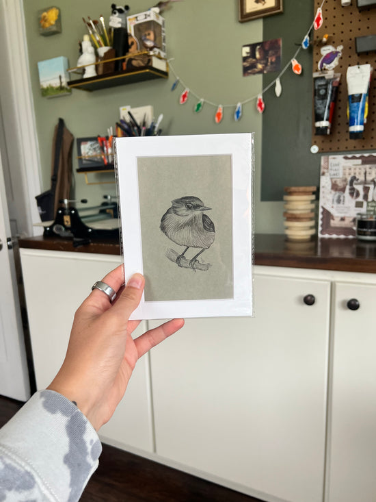 A hand holding a matted bird drawing.