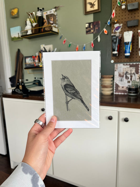 A hand holding a matted bird drawing.