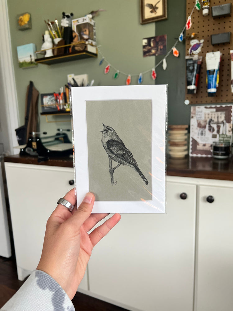 A hand holding a matted bird drawing.