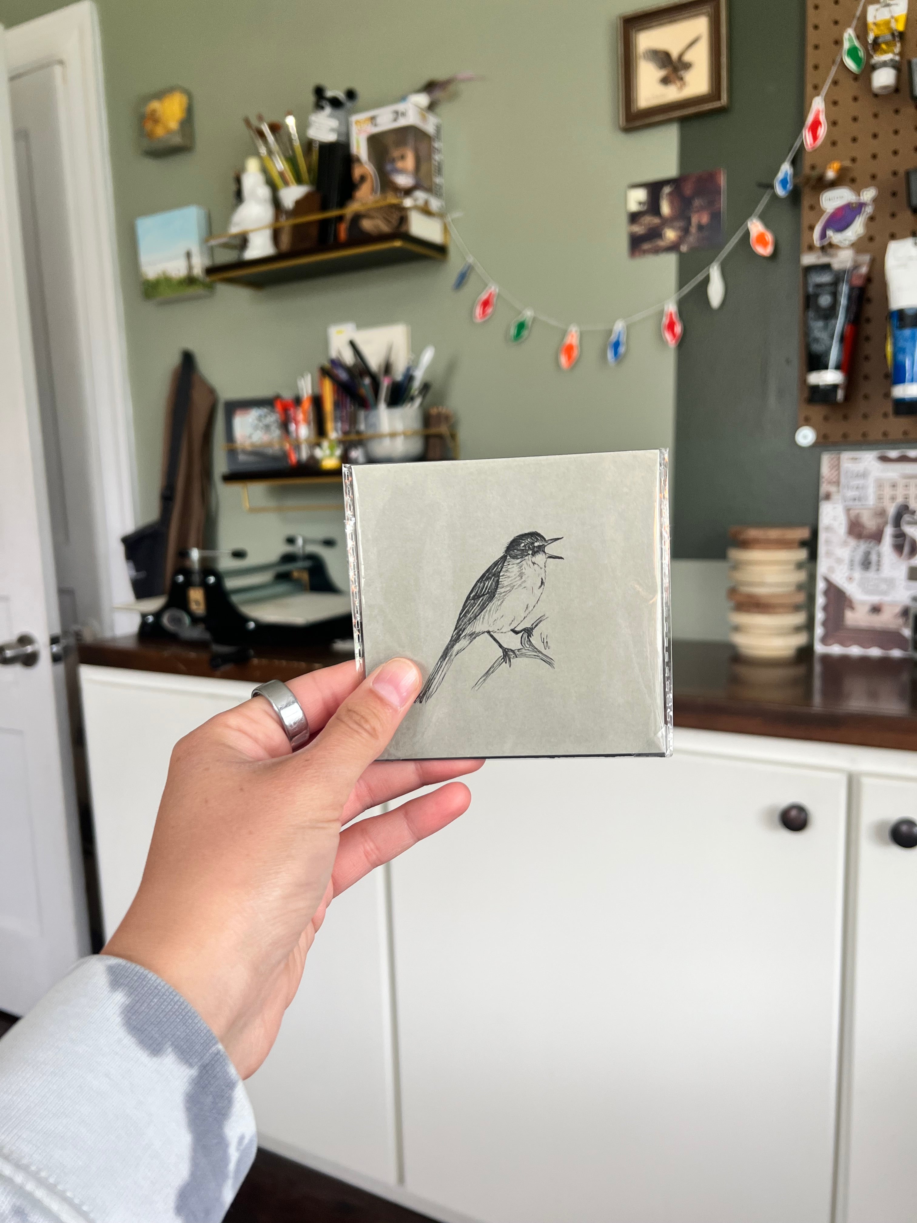 A hand holding a matted bird drawing.