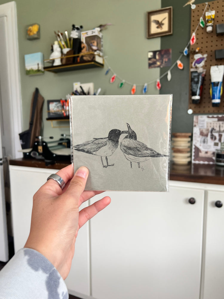 A hand holding a matted bird drawing.