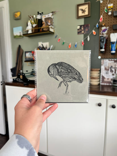 A hand holding a matted bird drawing.