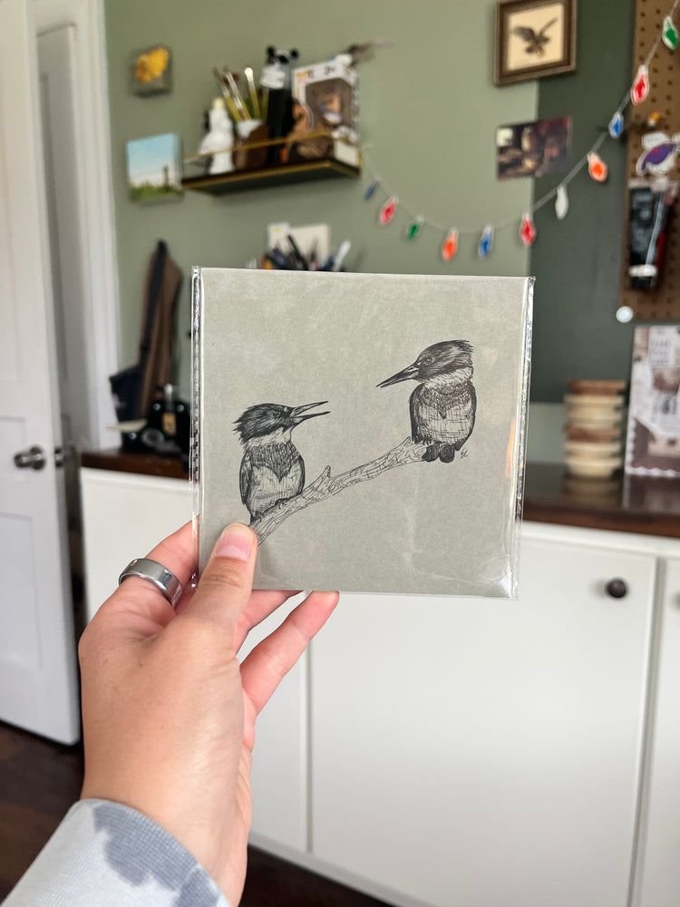 A hand holding a matted bird drawing.