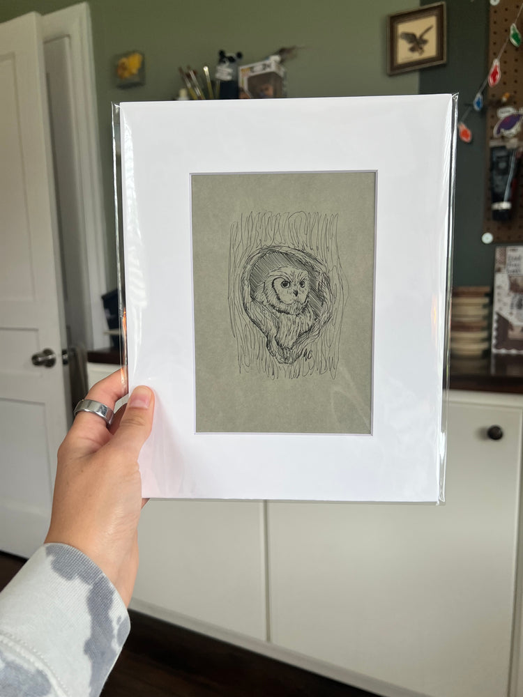 A hand holding a matted bird drawing.