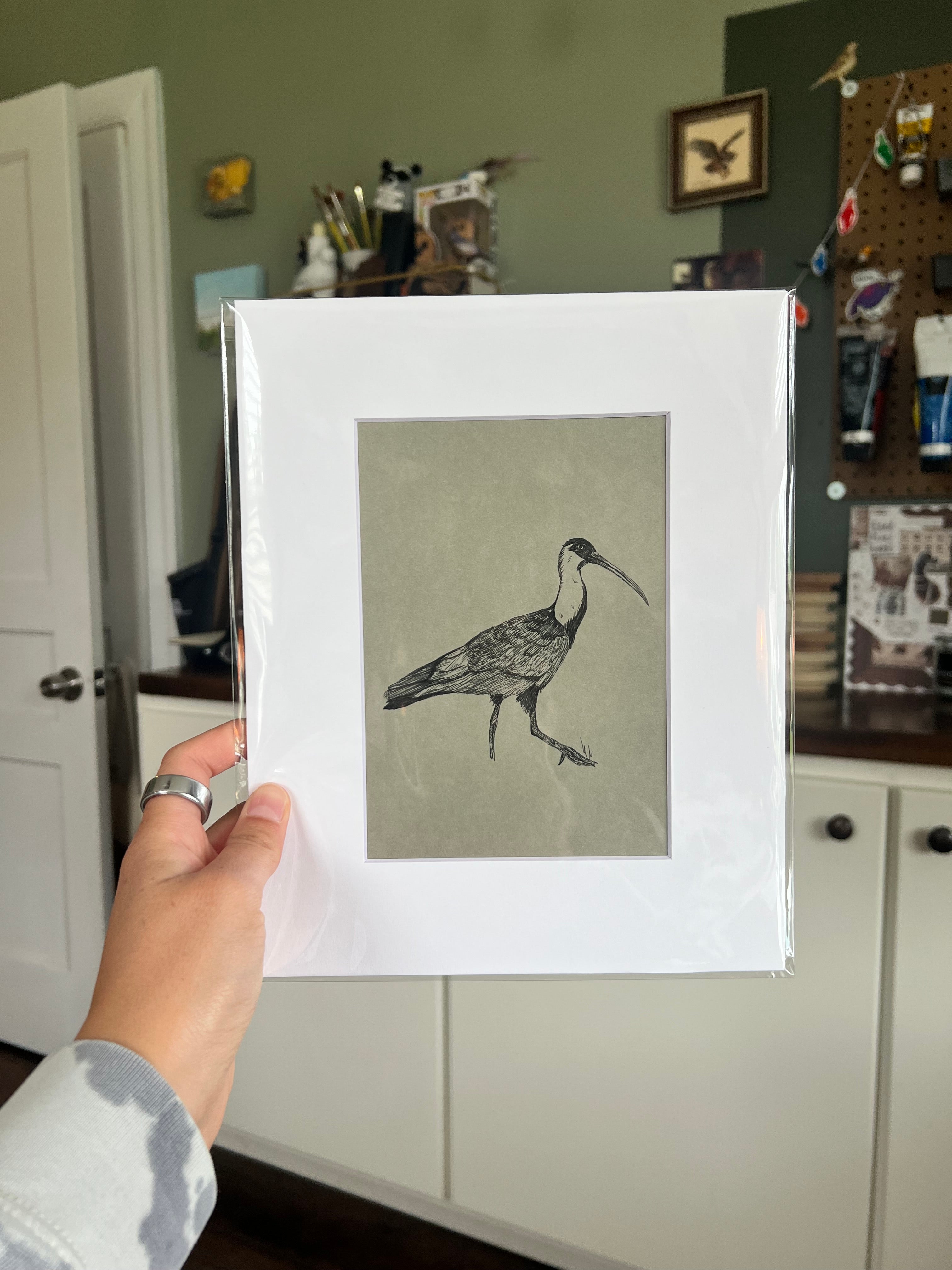 A hand holding a matted bird drawing.