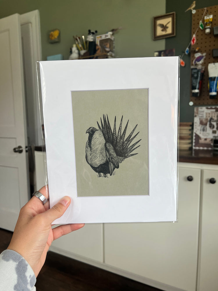 A hand holding a matted bird drawing.