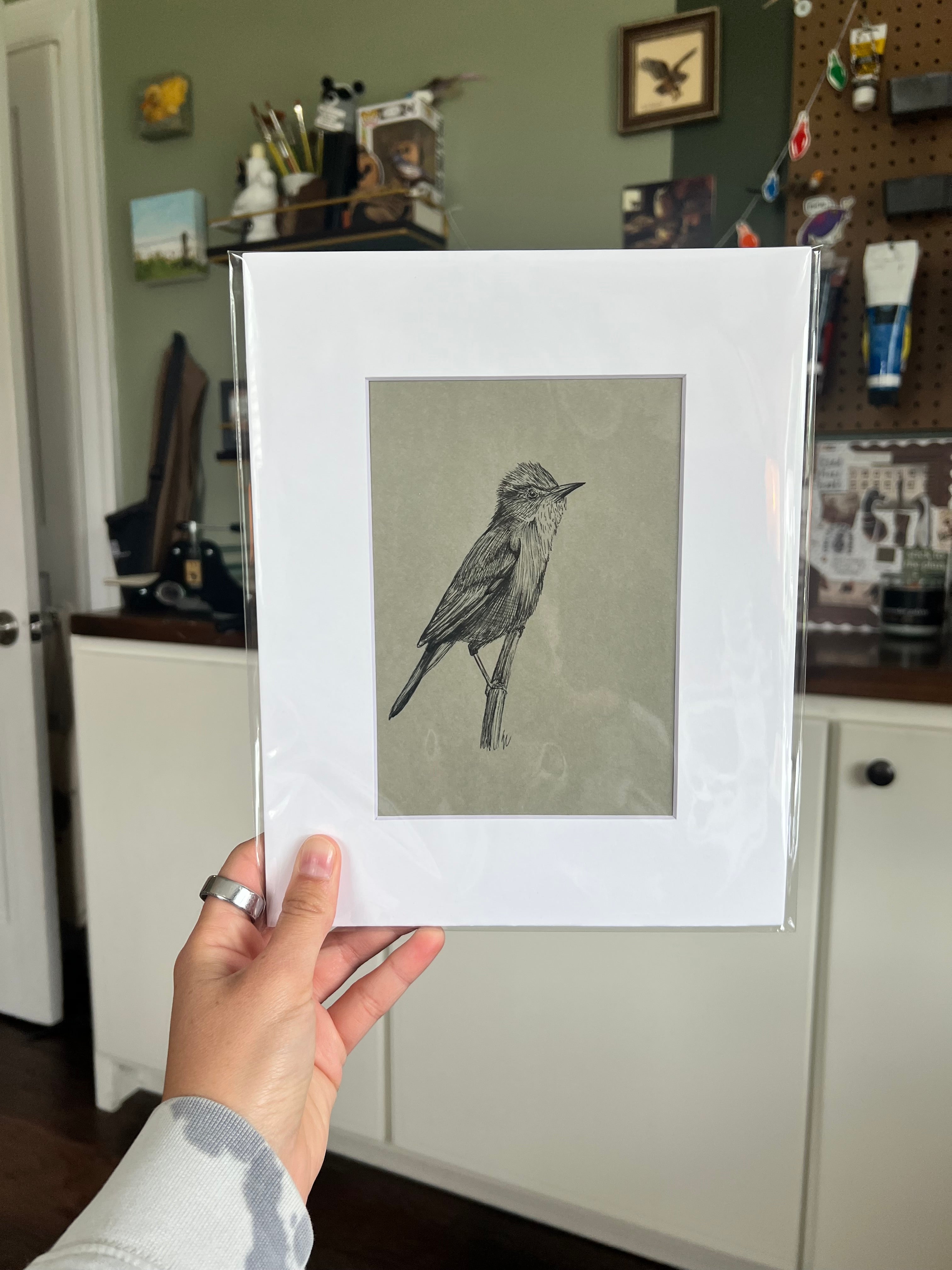 A hand holding a matted bird drawing.