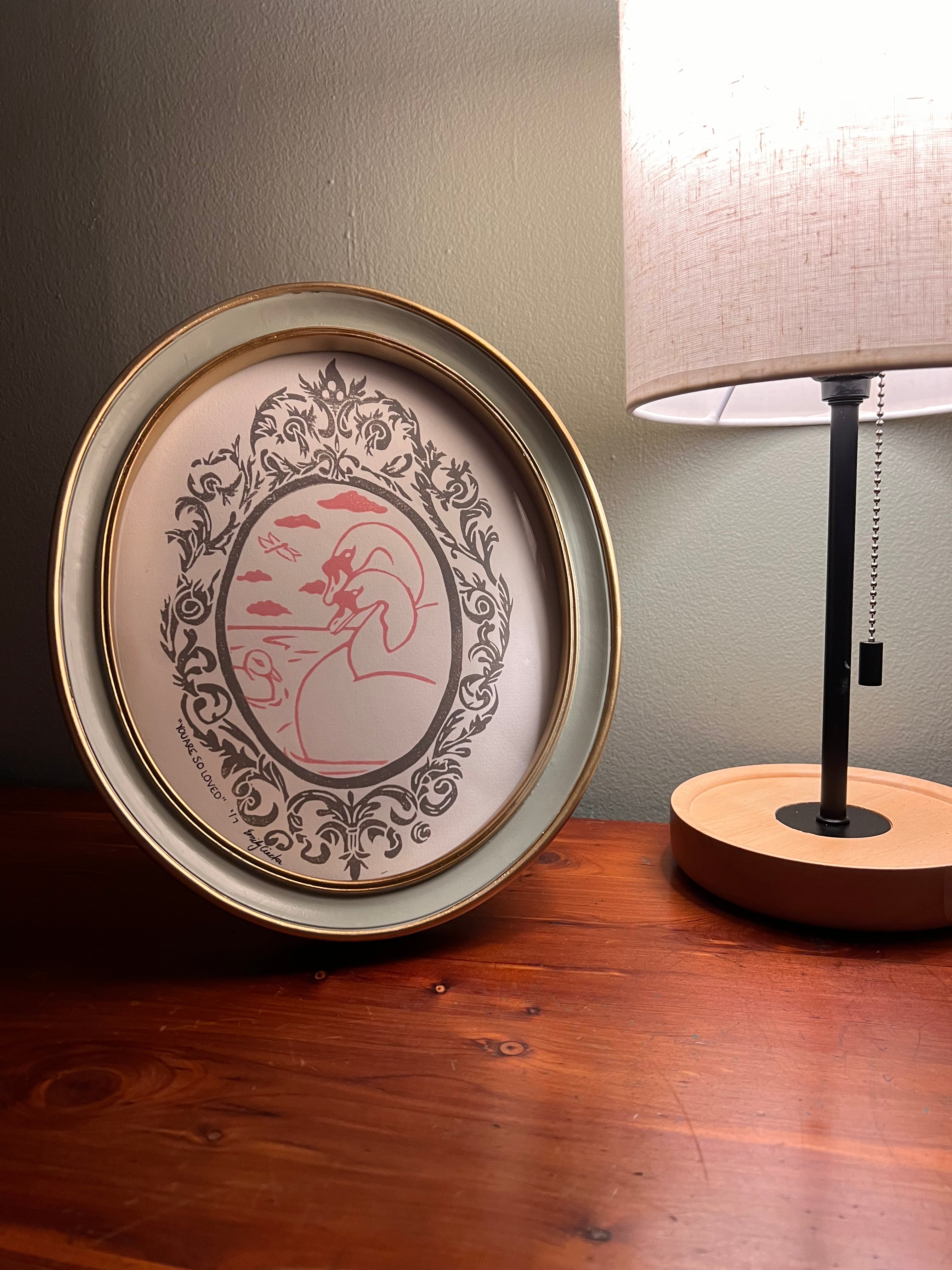 Framed artwork with lamp on a table.