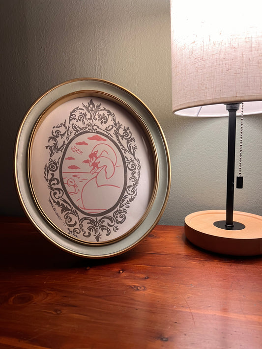 Framed artwork with lamp on a table.