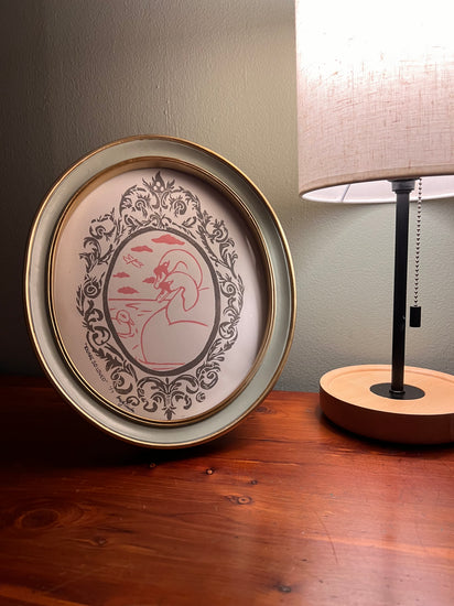 Framed artwork with lamp on a table.