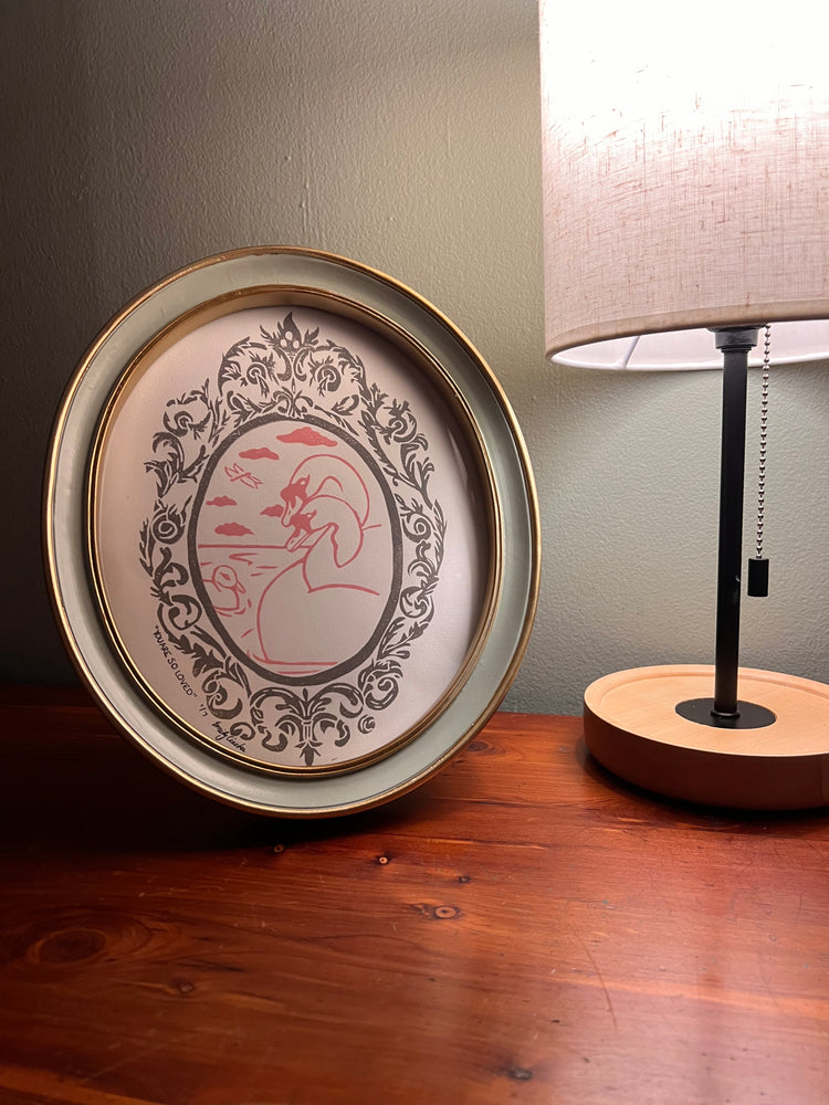 Framed artwork with lamp on a table.