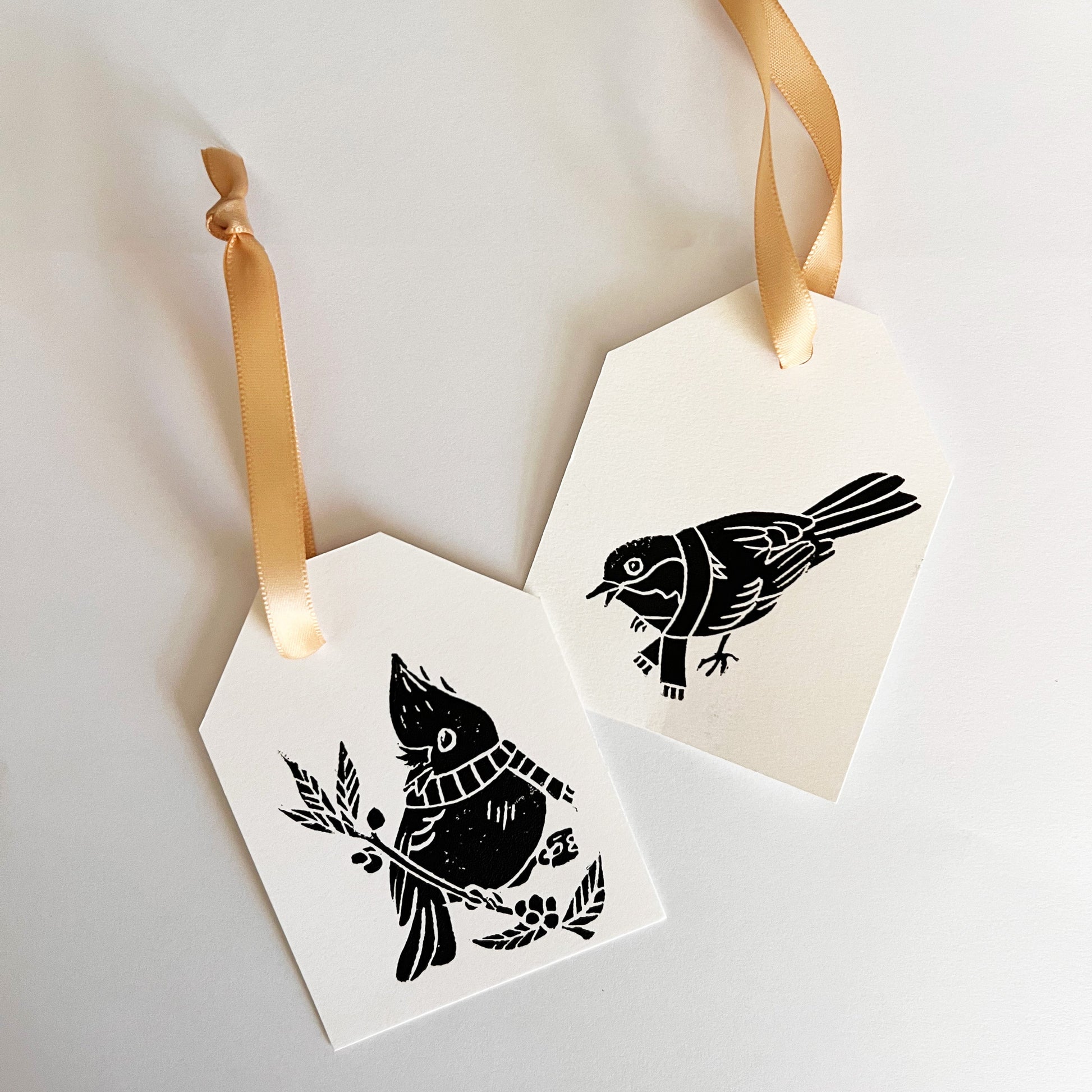 Two hexagonal gift tags with black bird illustrations and gold ribbons on a white background