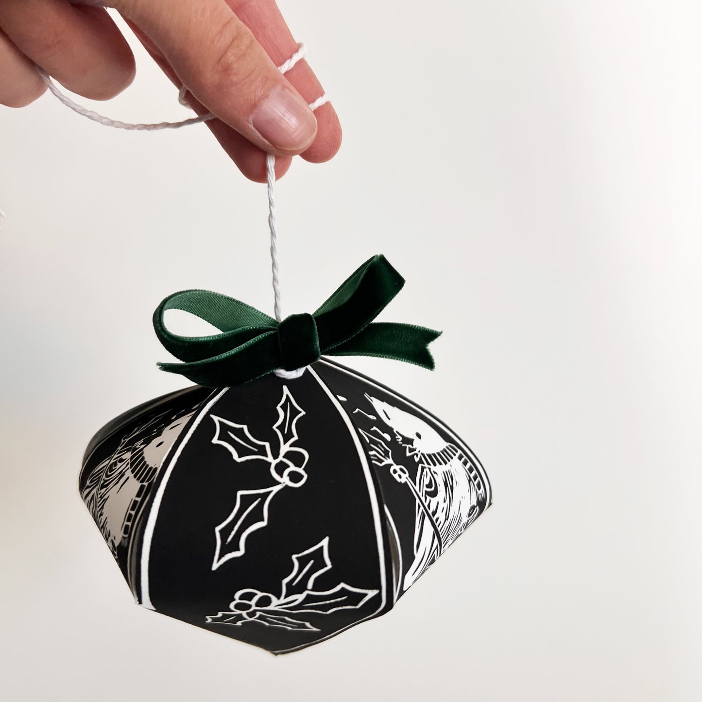 Black decorative box with white holly designs and a green ribbon, held by a hand against a light background.