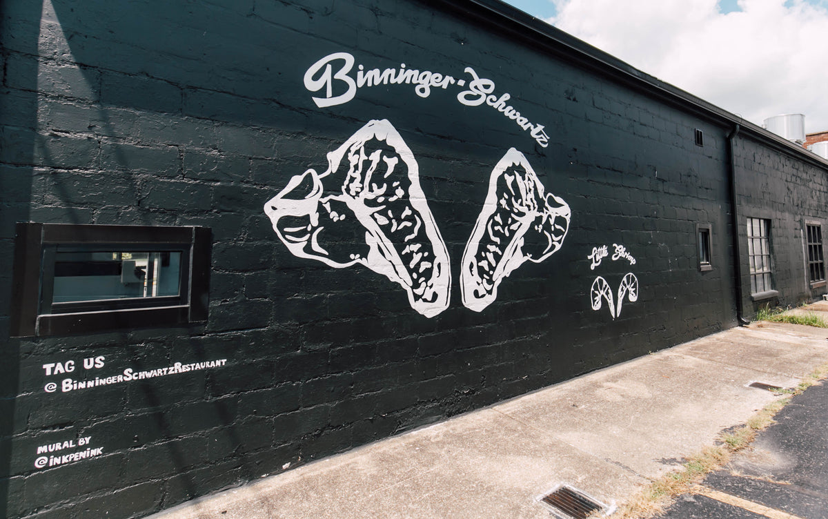 Black wall with white mural of steaks and shrimp with 'Binninger Schwartz' branding.